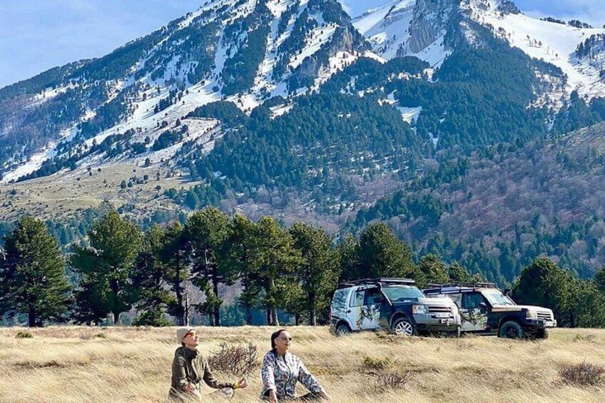 A mountainous landscape with snow-capped peaks, a field with dry grass, and two vehicles parked in the foreground. 4