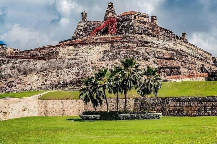 A historic fort with a grassy foreground and palm trees. 1