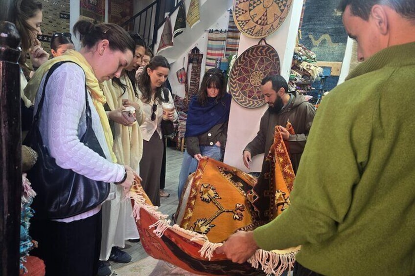 A group of people in a market, some holding bags and others looking at items on display. 2
