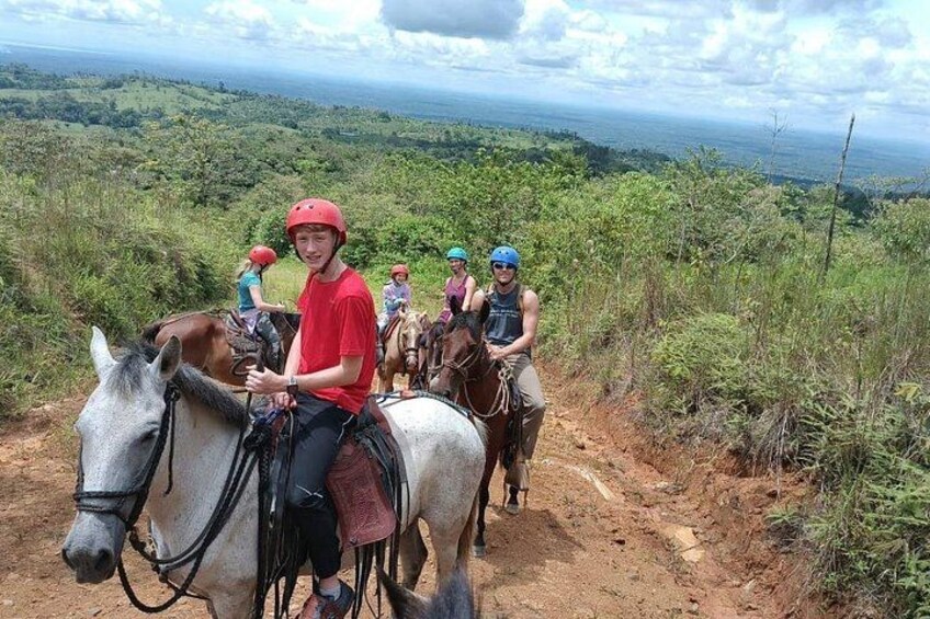 Un grupo de personas montando a caballo por un sendero de tierra rodeado de vegetación exuberante y colinas. 1