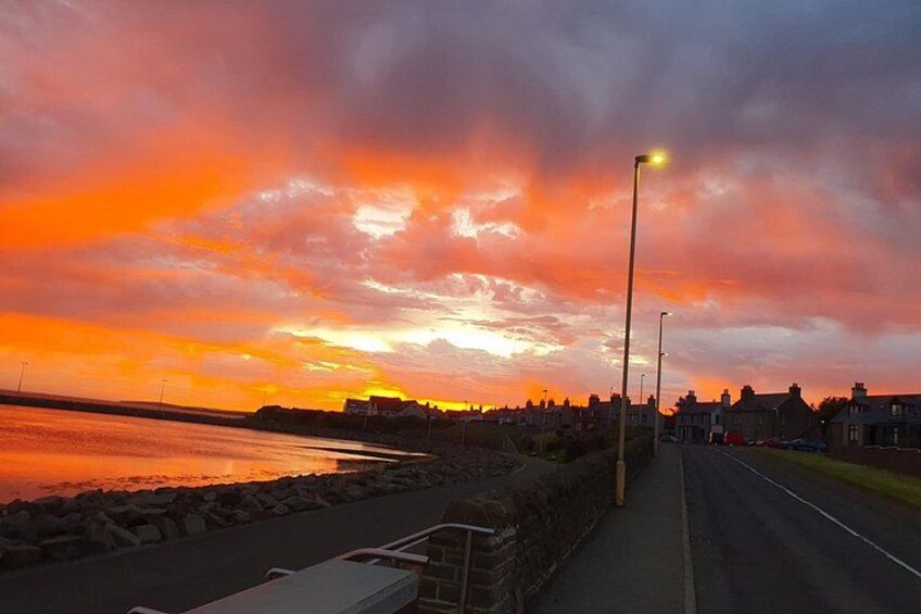 Un coucher de soleil sur une route côtière, avec un mur de pierres et des lampadaires. 3
