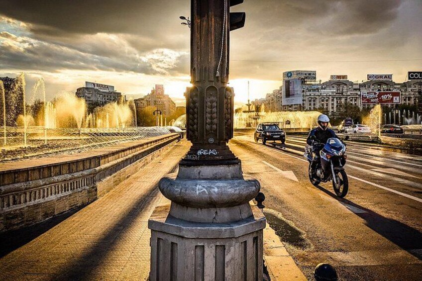 Un paisaje urbano con una fuente, una estatua y un motociclista sobre un puente. 3
