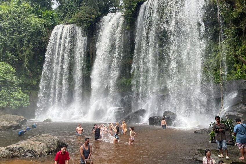 Une cascade composée de plusieurs ruisseaux, entourée d’une végétation luxuriante, où des personnes se baignent et profitent de l’eau. 5