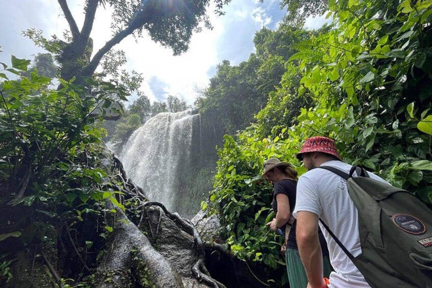 A waterfall surrounded by lush greenery, a person with a backpack, and another person in the background. 5