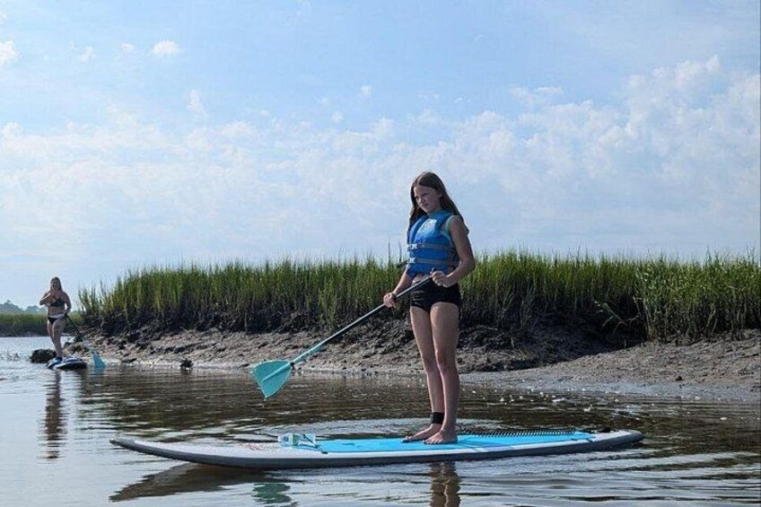 A person paddleboarding on a calm body of water with a grassy shoreline in the background. 3