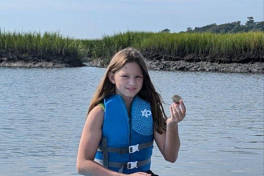A person holding a small object near a body of water with grass and trees in the background. 2