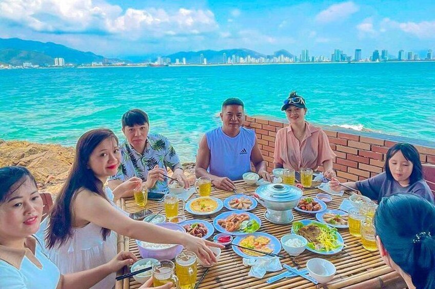 A group of people dining at a table with a view of the sea and a city skyline in the background. 2
