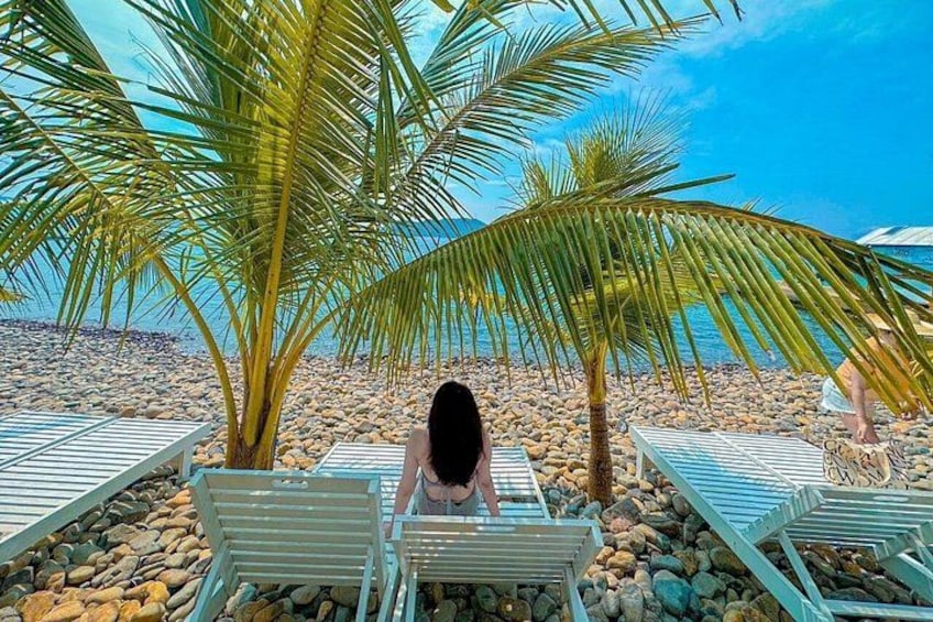 A beach with lounge chairs, palm trees, and a rocky shoreline. 4