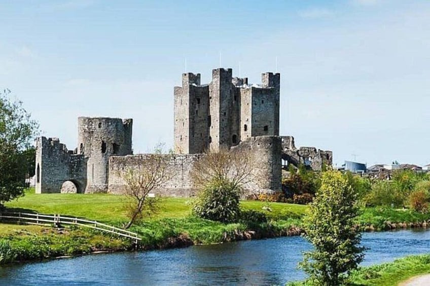 Un castillo histórico con múltiples torres, un río en primer plano y una zona verde con un pequeño puente. 4