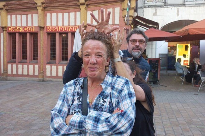 A person in a plaid shirt with crossed arms, another person behind them, and a building with signs reading 'Cafe Cul' and 'Restaurant' in the background. 3