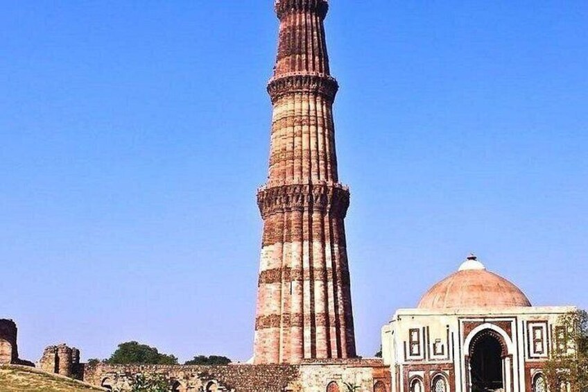 Een hoge minaret met een koepel, omgeven door oude ruïnes. 4