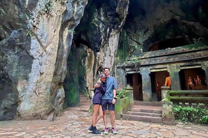 A couple standing in a cave-like structure with stone steps and a small shrine. 4