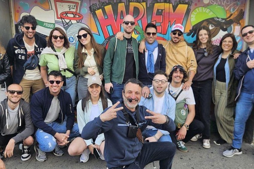Un grupo de personas posando frente a un mural colorido donde se lee la palabra 'HARMONI'. 2