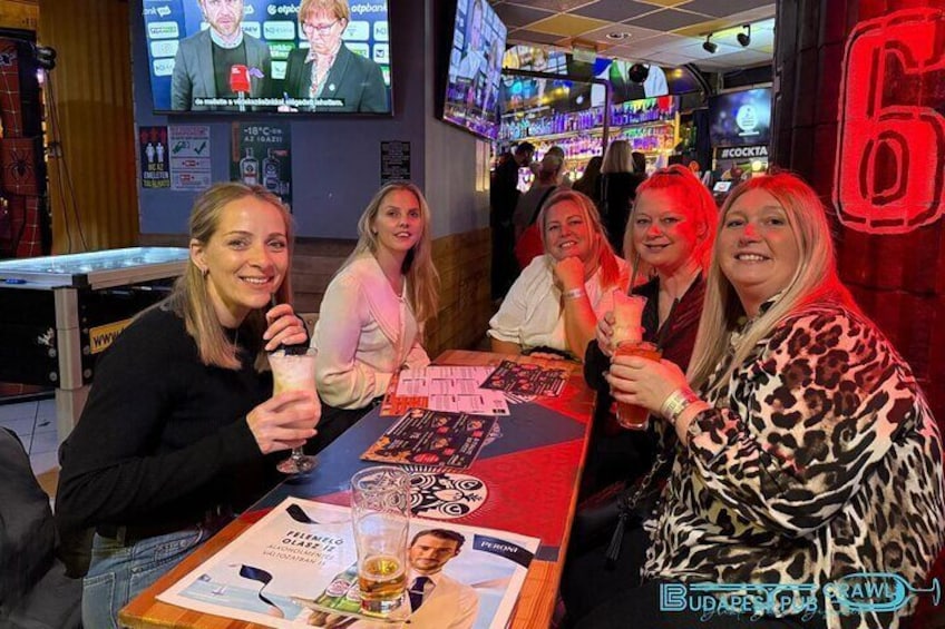 Eine Gruppe von Personen sitzt an einer Bar, im Hintergrund ein großes Schild mit der Zahl 6. 2