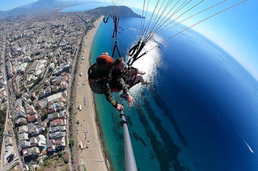 Eine Person gleitet mit einem Paragleiter über eine Küstenlandschaft mit Strand und Gebäuden. 5