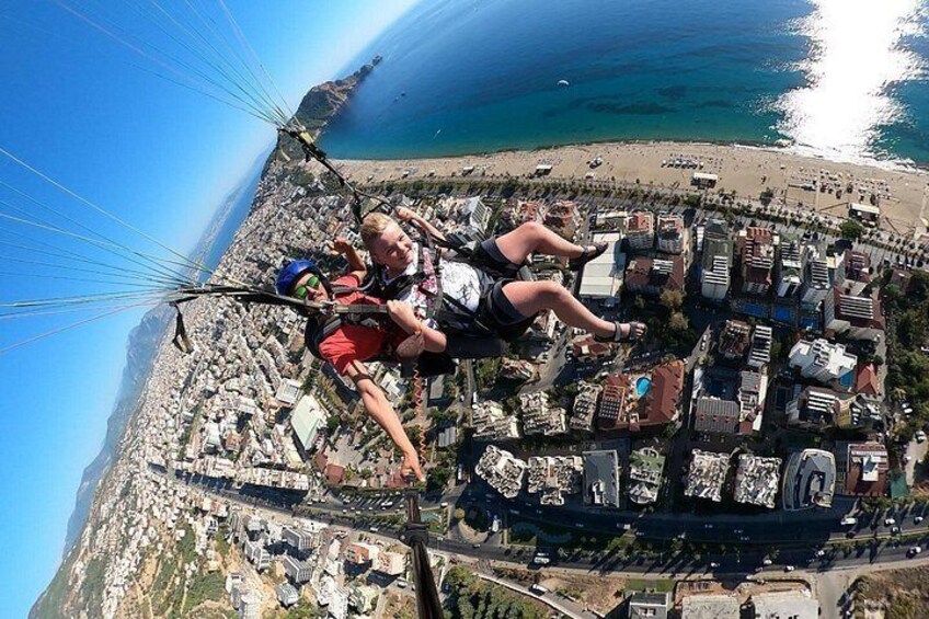Eine Person gleitet mit einem Paragleiter über einer Küstenstadt mit Gebäuden und einem Strand darunter. 4