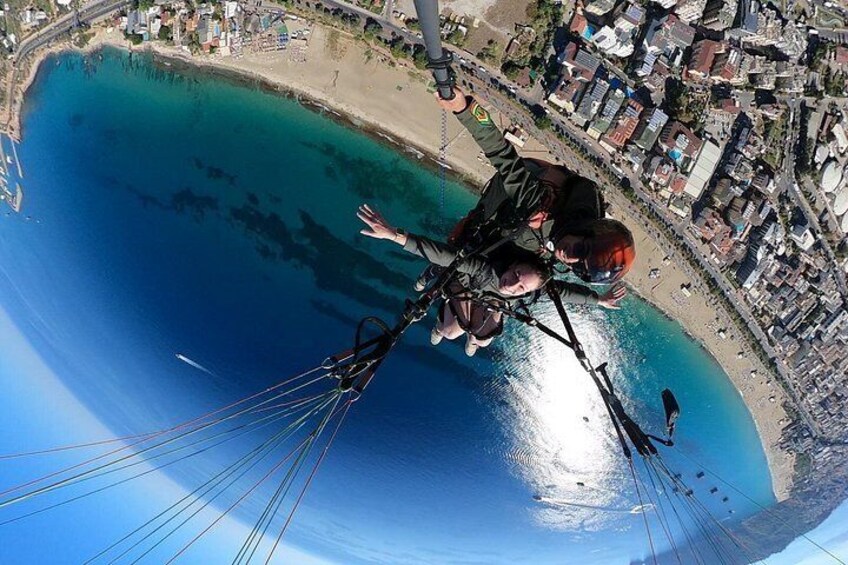 Eine Person macht Gleitflug über einer Küstenregion mit blauem Meer und einer Stadtlandschaft im Hintergrund. 3