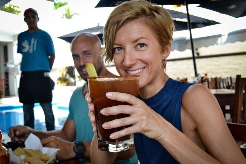 A person holding a drink with a straw, a table with food, and a beach in the background. 3