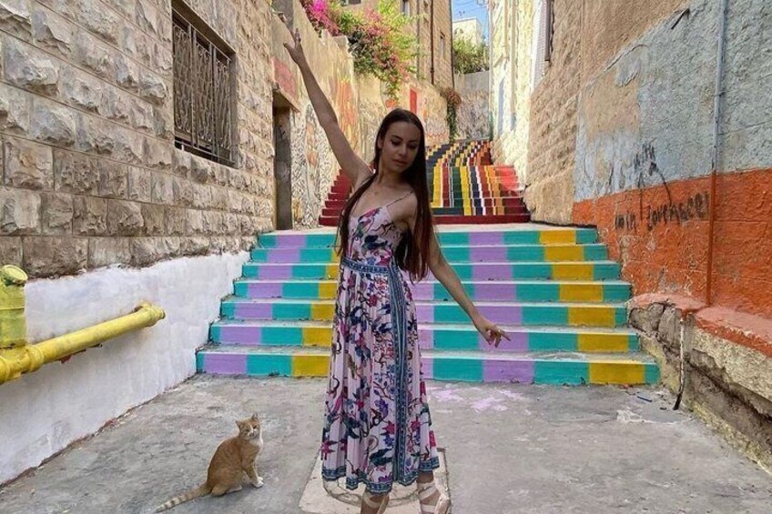 A person standing in a narrow alleyway with colorful steps leading up to a building. 4