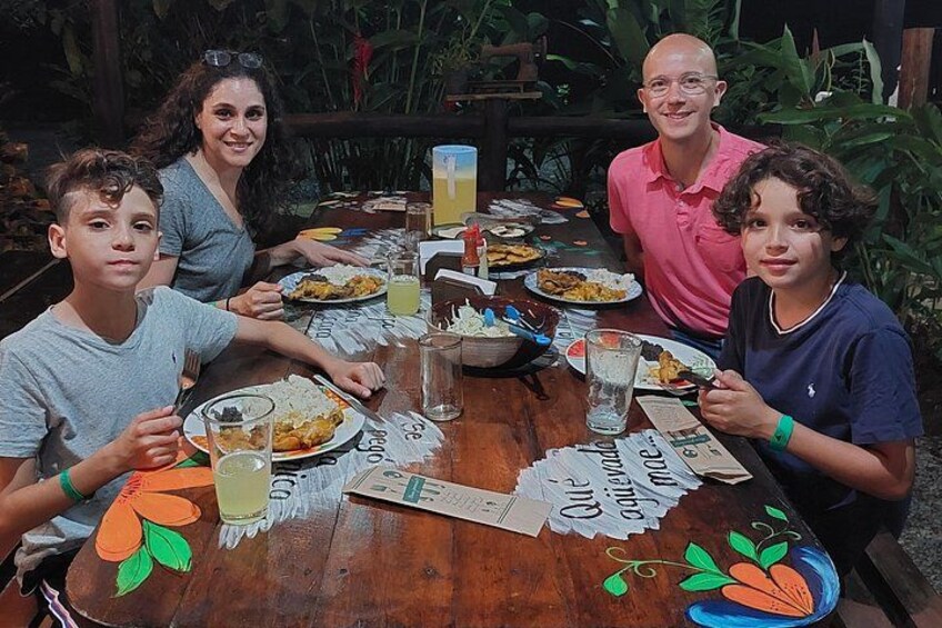 Une famille est assise autour d’une table en bois, devant des assiettes remplies de nourriture, des verres et un set de table orné d’un motif représentant une carotte. 4