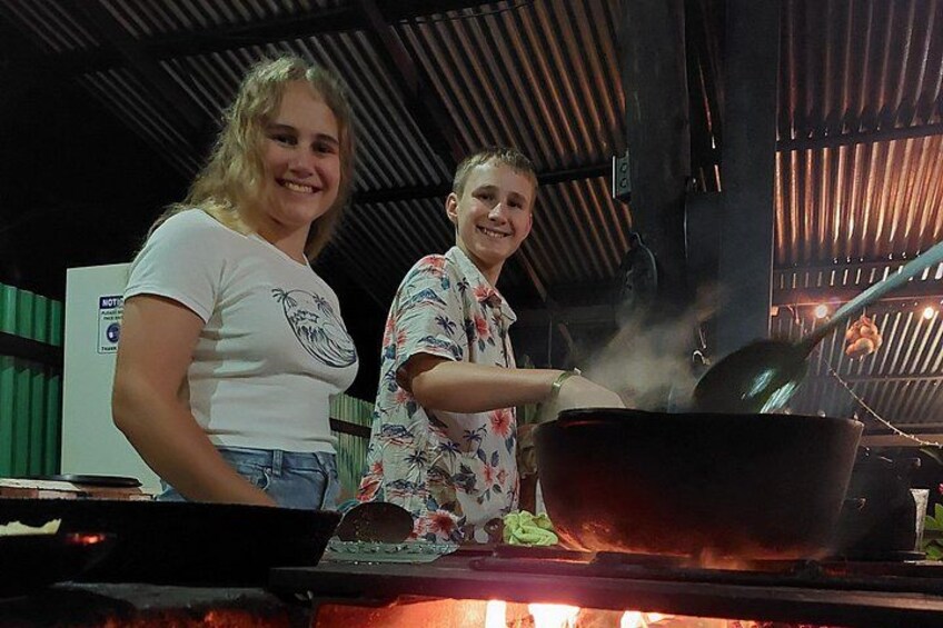 Deux personnes préparent un repas à l’extérieur, au-dessus d’un grand feu de camp. 5