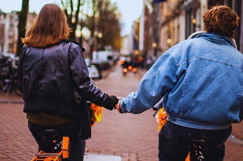 Two people walking down a street holding hands, with buildings and parked cars in the background. 2