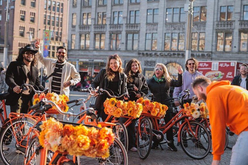 Un groupe de personnes à vélo, décorées d’éléments orange, se tient sur une rue de la ville. 2