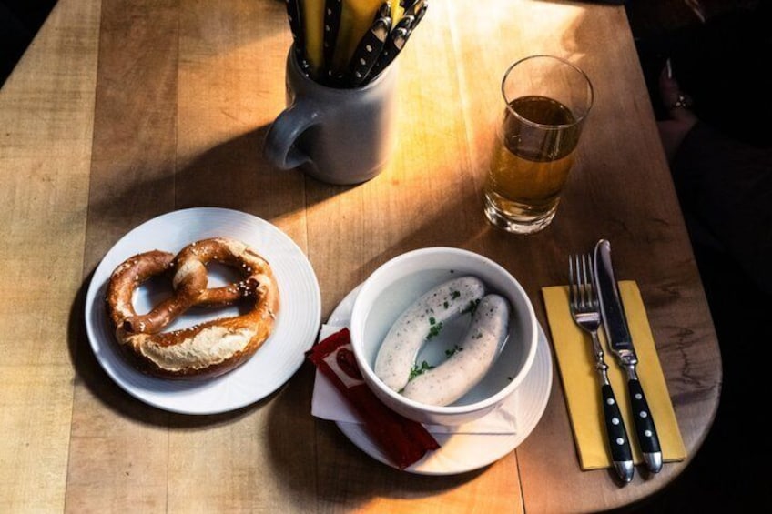 Un bretzel et un bol de soupe sur une table en bois, accompagnés d’un verre de bière et de couverts. 5