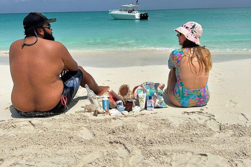 Two people sitting on a sandy beach with a boat in the background. 3