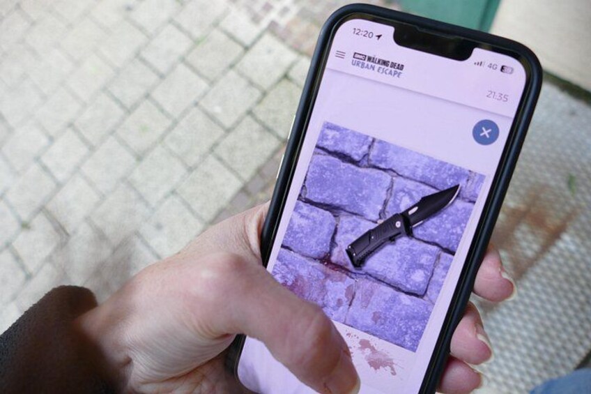 En hånd holder en smartphone, der viser et billede af en kniv mod en lilla murstensvæg. 1