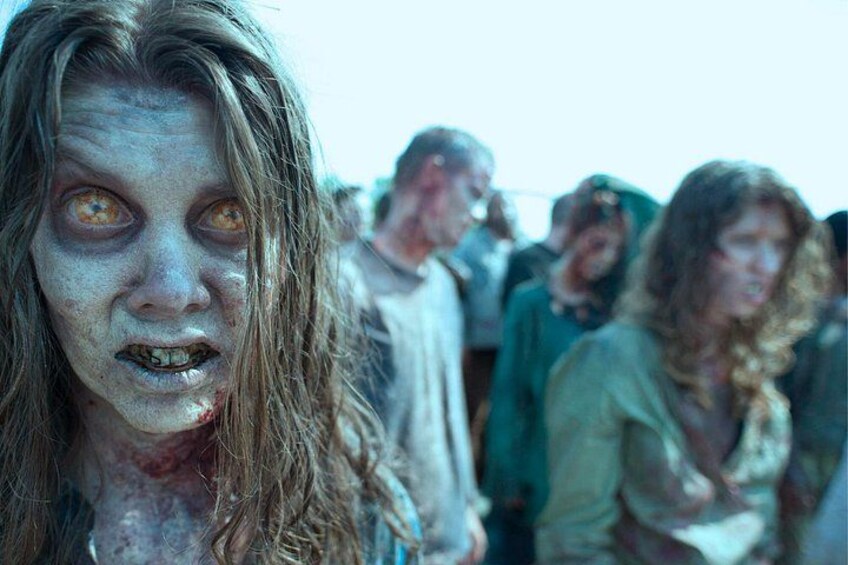 En person med udseende som en zombie, iført en hvid skjorte og grøn jakke, står i en menneskemængde. 2
