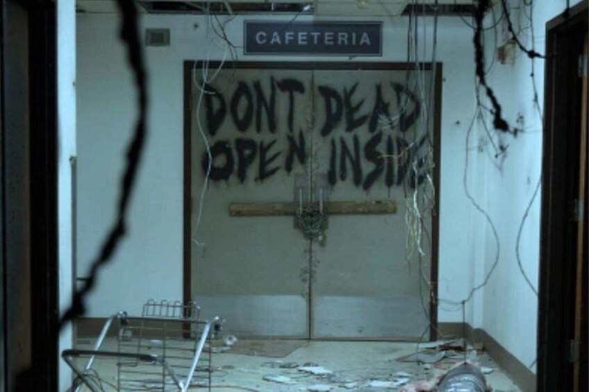 En lukket dør med graffiti-advarsel 'DON'T DEAD OPEN INSIDE' og et skilt over den, der siger 'CAFETERIA'. 5