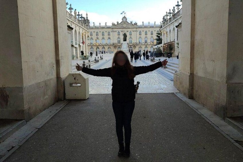 A person standing in a street with arms outstretched, facing a large historic building with columns and a grand entrance. 2