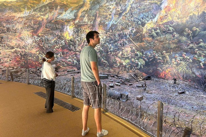 A man and a woman observing a large mural depicting a battle scene. 2