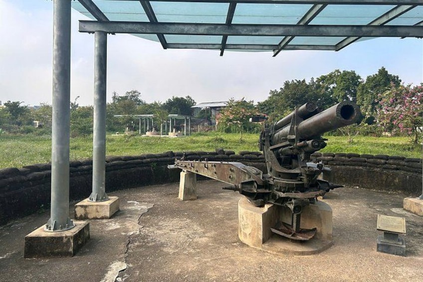 A large artillery piece in an open field with a metal shelter overhead. 4