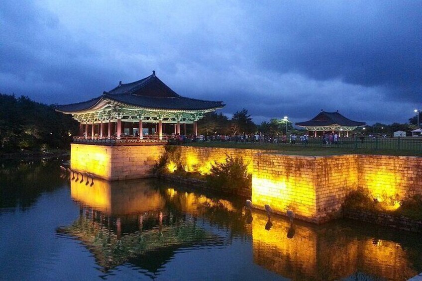 A traditional pavilion by a calm water body, reflecting the structure and a cloudy sky. 2