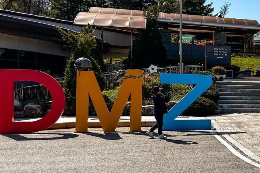 Large letters 'DMZ' in red, yellow, and blue colors, with a person standing in front of them. 3