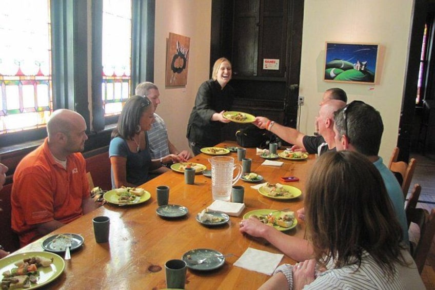 Een groep mensen zit rond een houten tafel, met borden eten, glazen en een karaf. 3