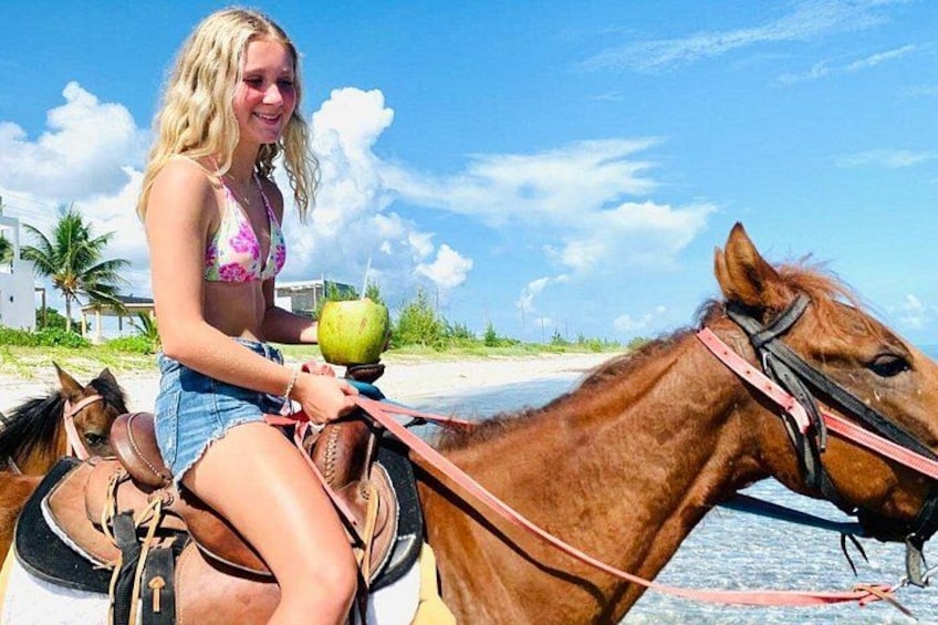 A person riding a horse on a beach with a coconut in hand. 1