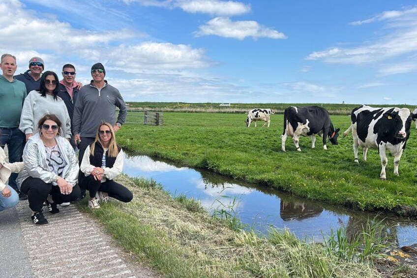 Un grupo de personas posando junto a un canal, con vacas pastando al fondo. 3