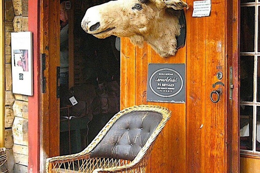 A wooden door with a mounted animal head, a wicker chair, and a plaque with text. 5