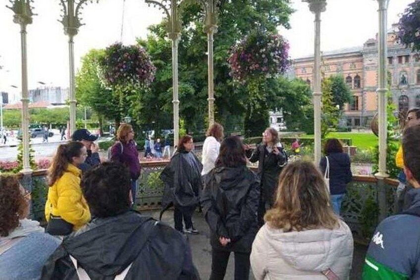 A group of people gathered in a park with a gazebo and hanging flower baskets. 4