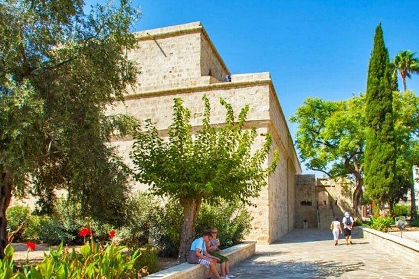 A stone building with a tree in front, a pathway, and a person sitting on a bench. 1