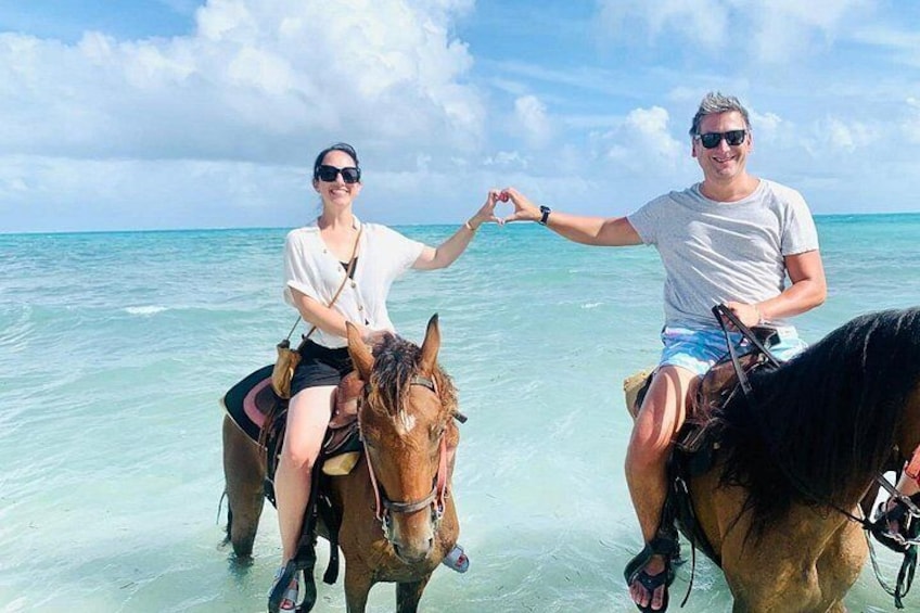 Twee mensen ríjdend op paarden aan een strand, met helder water en een blauwe lucht. 4