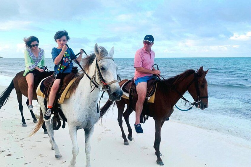 Three people riding horses on a beach with the ocean in the background. 2