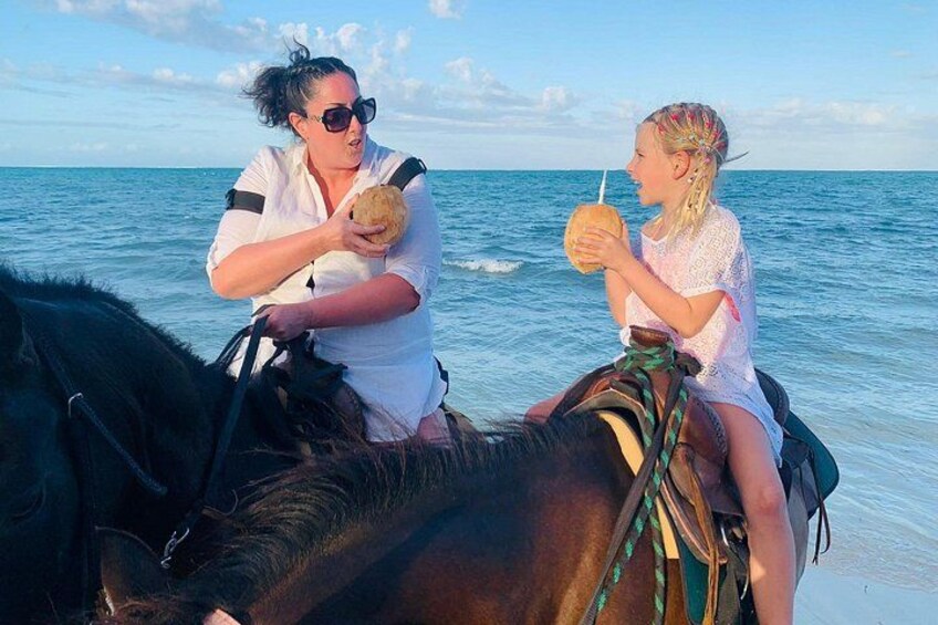 Two people on horseback by the sea, one holding a coconut. 1