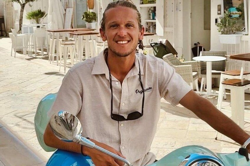 A person sitting on a scooter in an outdoor café setting. 1