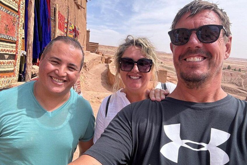 Three people standing in a desert landscape with buildings in the background. 5