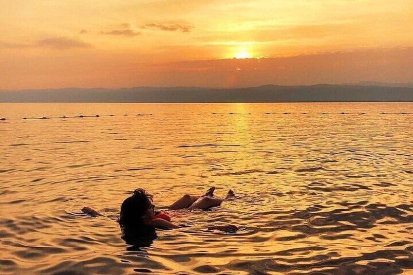 Een zonsondergang boven een rustige zee, met iemand en een hond in het water. 2