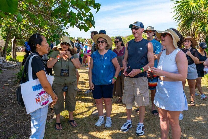 A group of people standing outdoors, some wearing hats and sunglasses, with trees and a clear sky in the background. 2